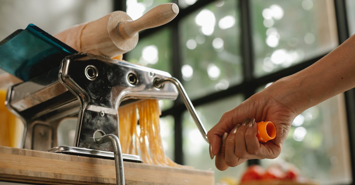Pasta edges break when being rolled in pasta machine - Crop woman using pasta machine Pasta edges break when being rolled in pasta machine - Crop woman using pasta machine