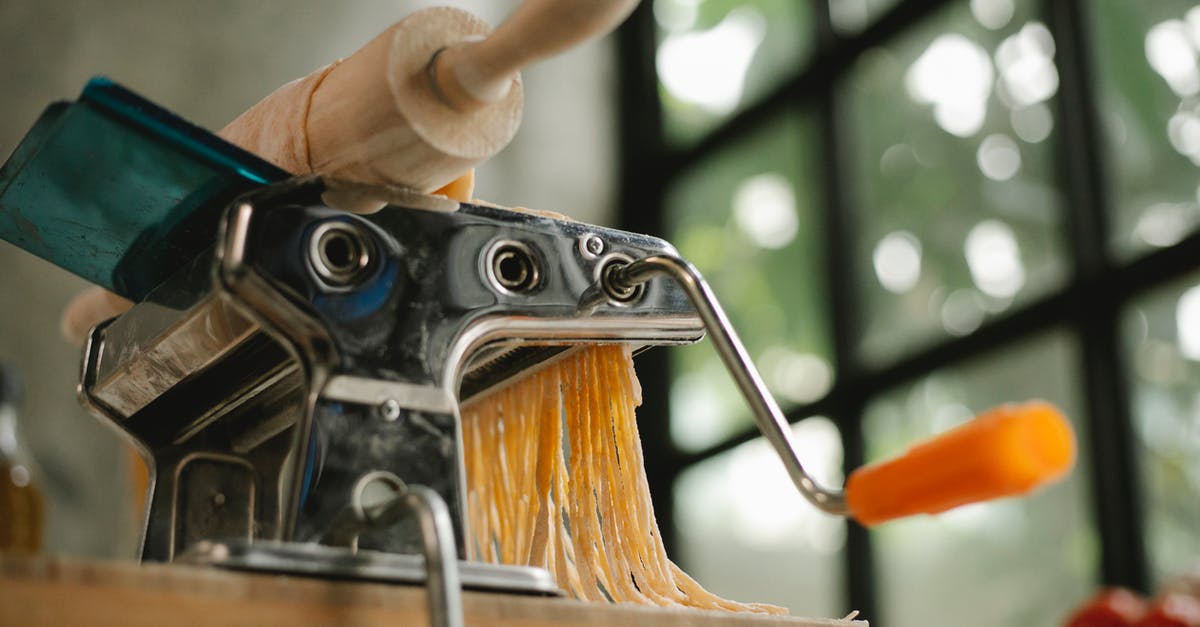 Pasta sticks to rolling cutters - From below of modern stainless pasta maker equipment with cut raw dough placed on wooden table in kitchen on blurred background Pasta sticks to rolling cutters - From below of modern stainless pasta maker equipment with cut raw dough placed on wooden table in kitchen on blurred background