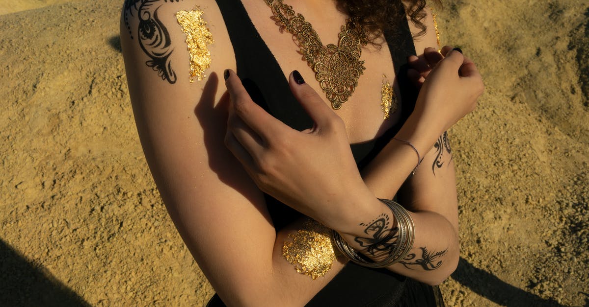 Pattern in carrot's body - Crop anonymous female with tattoos and curly hair in black top standing with hands crossed in sand area