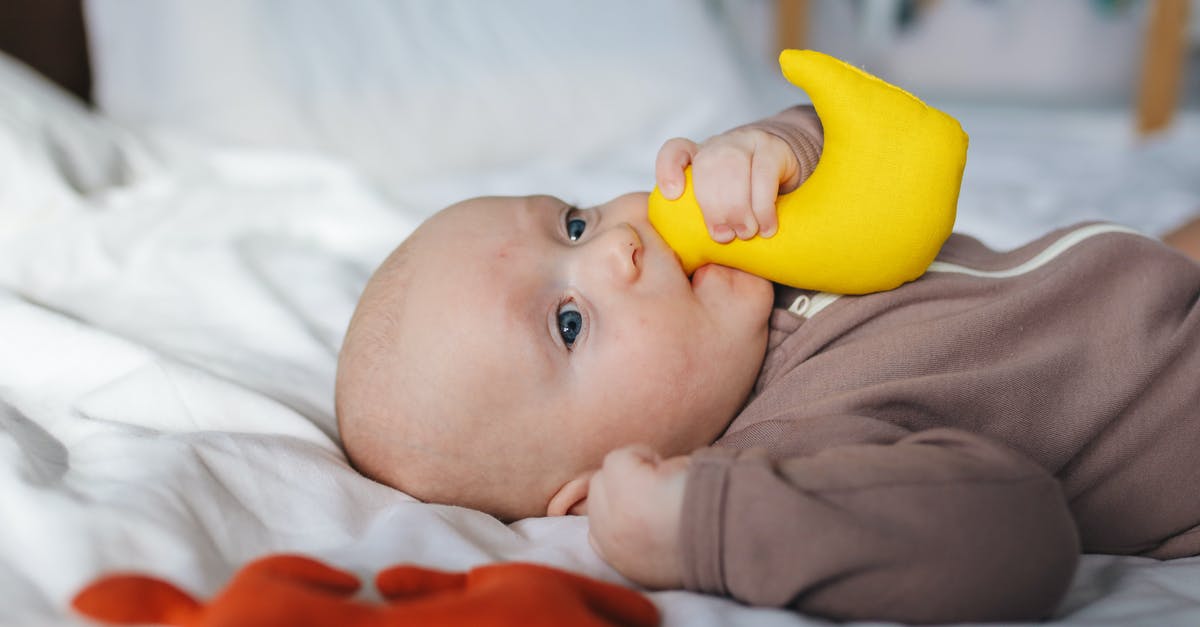 Peking Duck - why do they take my duck away? - Side view of adorable newborn in brown wear lying on bed with clenched fist and yellow toy in mouth Peking Duck - why do they take my duck away? - Side view of adorable newborn in brown wear lying on bed with clenched fist and yellow toy in mouth