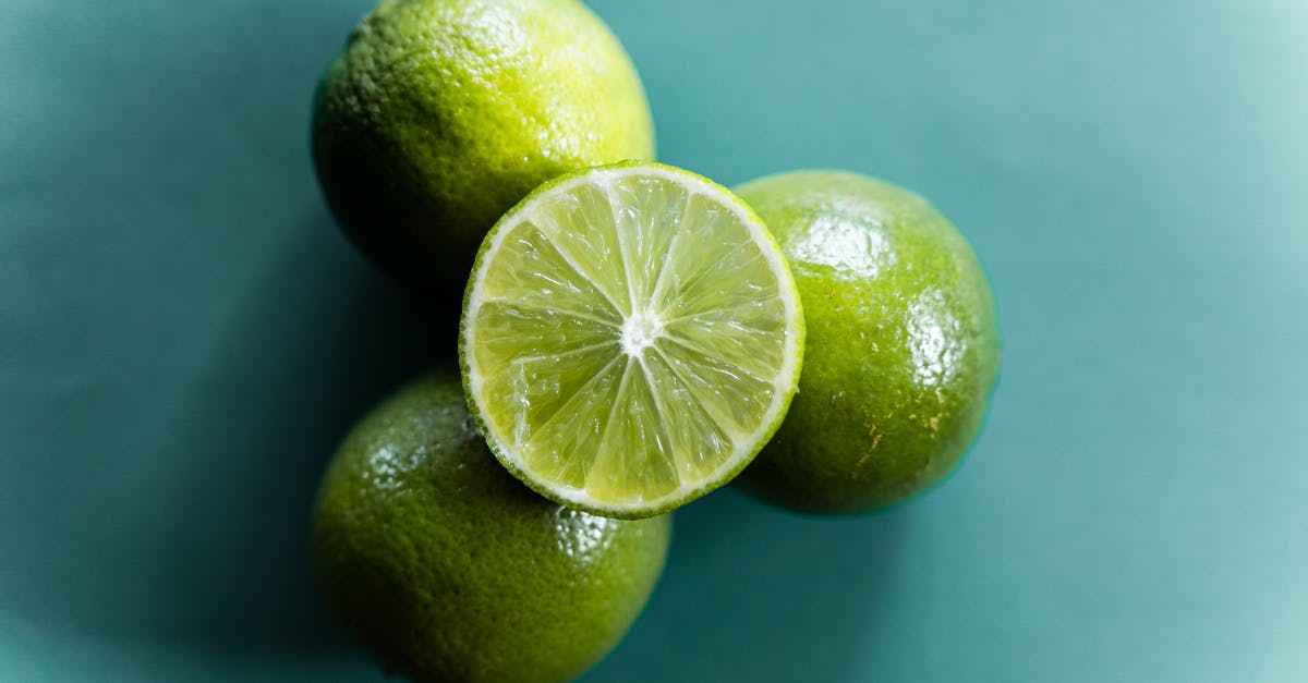 Post harvest treatment of organic limes vs conventional limes - Top view of fresh ripe halved and whole limes stacked on green background Post harvest treatment of organic limes vs conventional limes - Top view of fresh ripe halved and whole limes stacked on green background