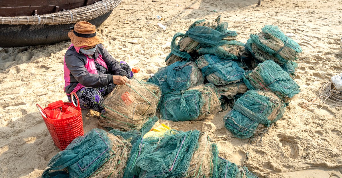 Prevent gummi bears from drying out - From above of anonymous ethnic female in hat and mask tying fishing net against oriental boats on beach in sunlight Prevent gummi bears from drying out - From above of anonymous ethnic female in hat and mask tying fishing net against oriental boats on beach in sunlight