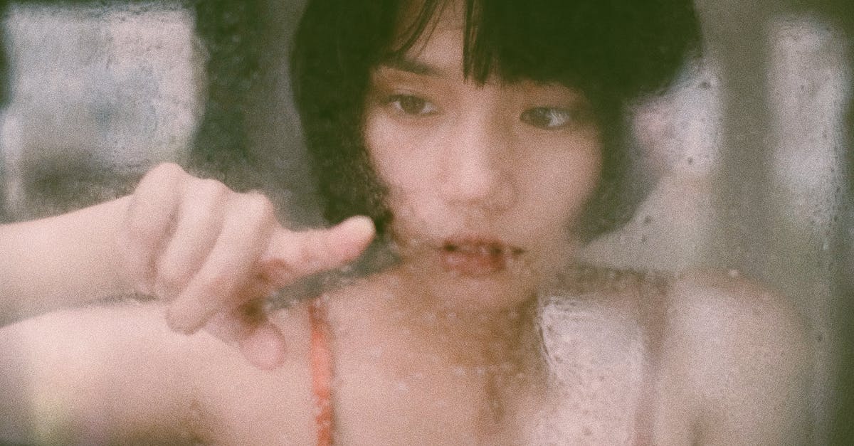 Puff Pastry wet / gummy on the inside - Through window of young Asian woman drawing on wet glass with finger in soft light Puff Pastry wet / gummy on the inside - Through window of young Asian woman drawing on wet glass with finger in soft light