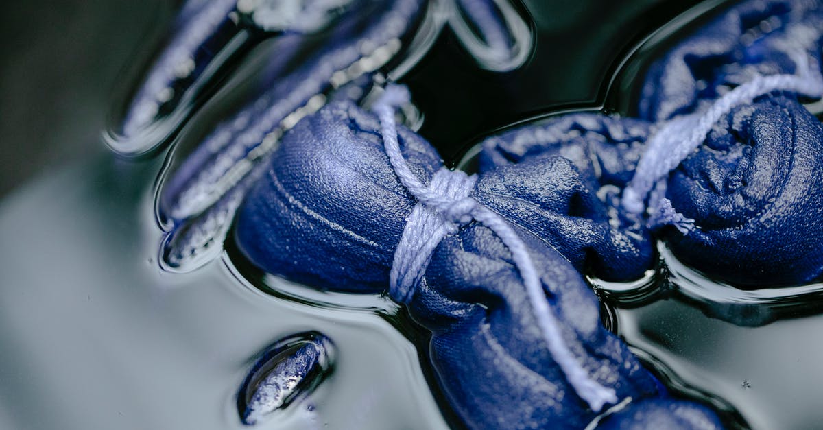 Pumpkin Roll Technique - From above rolls of fabric tied with ropes placed in liquid with paint on blurred background in modern workshop using shibori technique