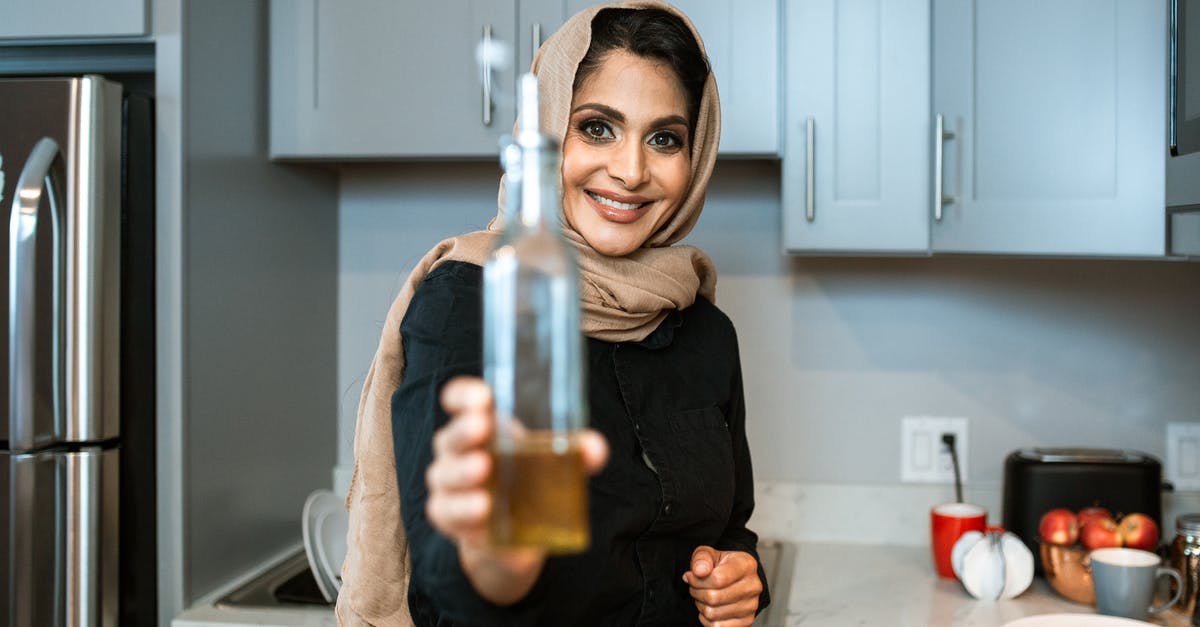Recipes say not to boil butter for beurre monté - why? - Happy ethnic female in headscarf showing bottle of organic olive oil and looking at camera with smile while cooking in contemporary kitchen Recipes say not to boil butter for beurre monté - why? - Happy ethnic female in headscarf showing bottle of organic olive oil and looking at camera with smile while cooking in contemporary kitchen
