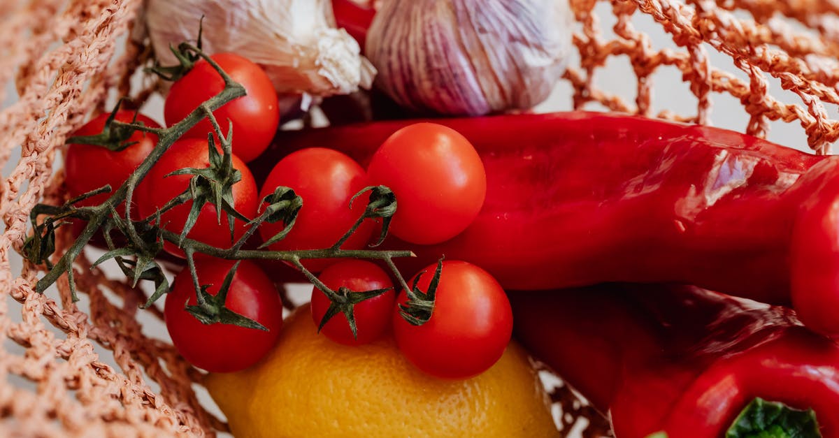 Reduce spiciness of chili [duplicate] - Top view of ripe tomatoes on branch arranged amidst fresh yellow lemon and red chili peppers with garlic in pink food net