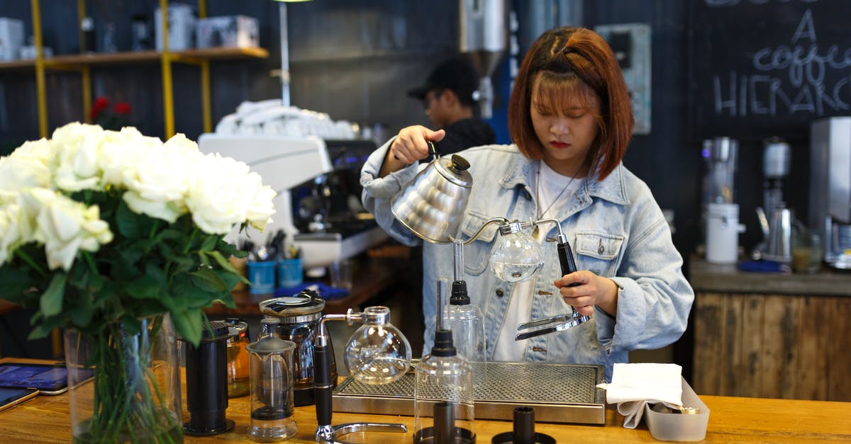 Reducing stock and then adding water - Woman Holding Kettle While Standing at the Table Reducing stock and then adding water - Woman Holding Kettle While Standing at the Table