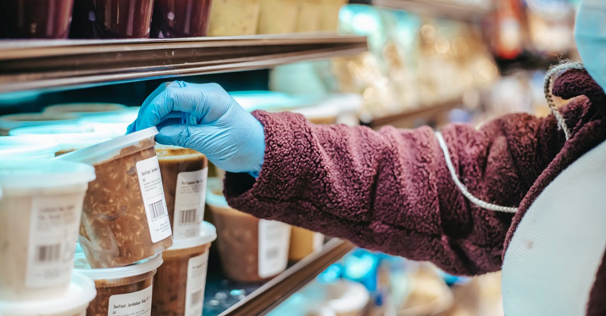 References on food safety? - Crop anonymous female customer in protective mask reading label on frozen food in plastic container in grocery store References on food safety? - Crop anonymous female customer in protective mask reading label on frozen food in plastic container in grocery store
