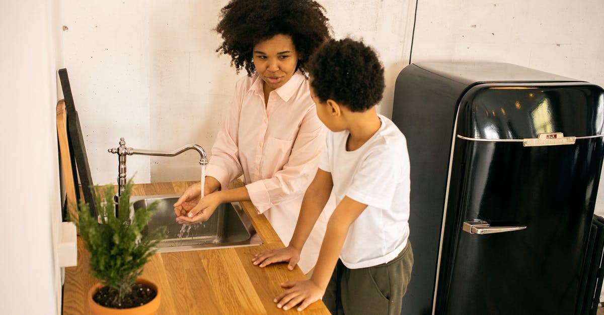 Refrigerator drips water inside - African American mother with son washing hands while standing at sink near green potted plant in kitchen with black refrigerator Refrigerator drips water inside - African American mother with son washing hands while standing at sink near green potted plant in kitchen with black refrigerator
