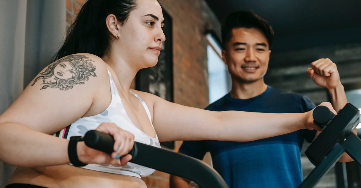 Removing fat from a recipe - From below of happy young Asian male trainer motivating exhausted young female client to to cardio fat burning exercise on elliptical machine in modern sport club Removing fat from a recipe - From below of happy young Asian male trainer motivating exhausted young female client to to cardio fat burning exercise on elliptical machine in modern sport club
