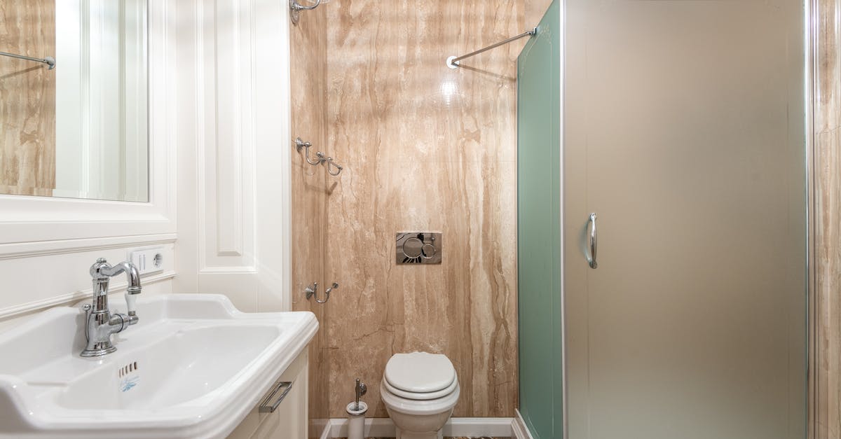 Residue on a new hard-nitriding cast iron skillet - Interior of bathroom with wall mounted toilet and shower cabin at tiled wall near clean sink under bright lighting Residue on a new hard-nitriding cast iron skillet - Interior of bathroom with wall mounted toilet and shower cabin at tiled wall near clean sink under bright lighting
