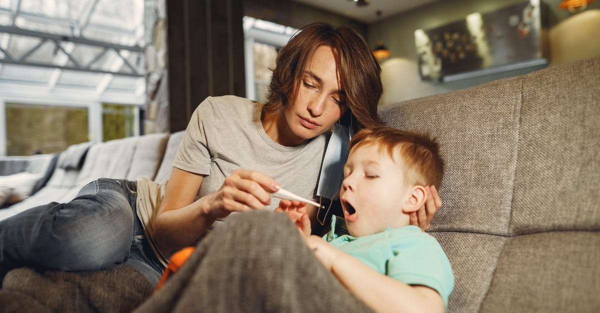 Resting meat - room temperature and bacteria - Mother taking sons temperature while sitting on sofa in apartment Resting meat - room temperature and bacteria - Mother taking sons temperature while sitting on sofa in apartment