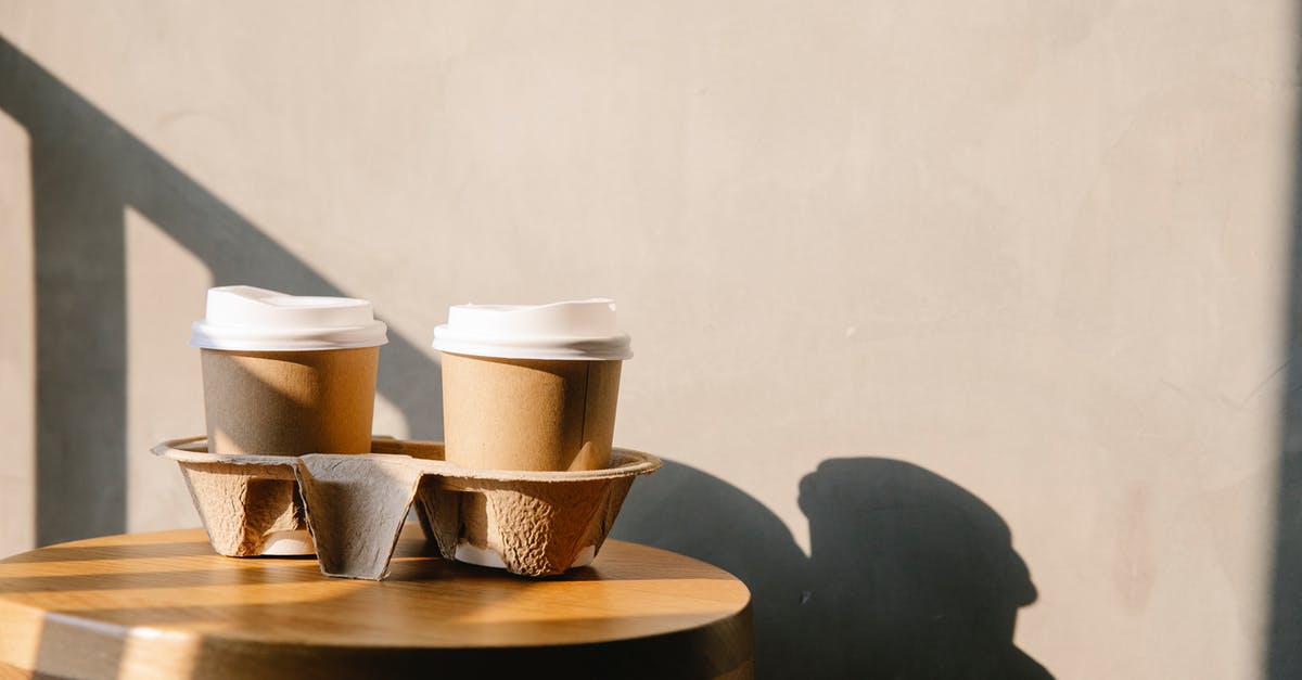 Reusing coffee grounds - Cofee paper cups with plastic lids on holder tray on brown wooden table casting a shadow at sunny day Reusing coffee grounds - Cofee paper cups with plastic lids on holder tray on brown wooden table casting a shadow at sunny day