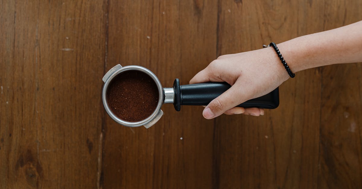 Reusing coffee grounds - Top view of crop unrecognizable barista hand with metal portafilter full of aromatic ground coffee against wooden shabby table Reusing coffee grounds - Top view of crop unrecognizable barista hand with metal portafilter full of aromatic ground coffee against wooden shabby table