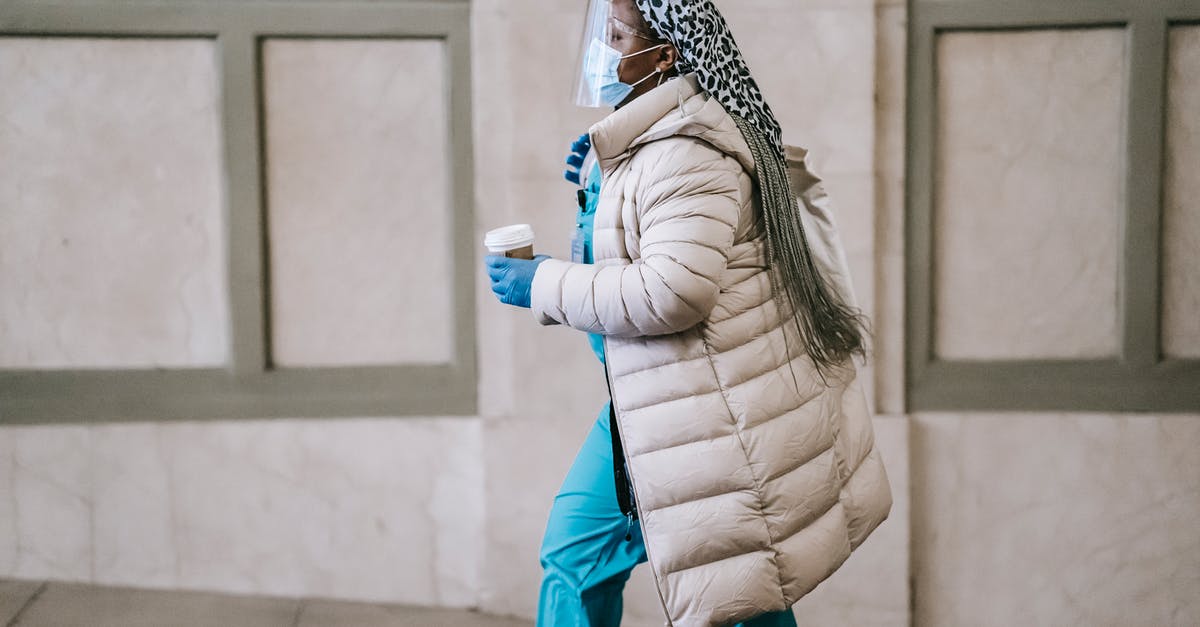 rice warming & safe - Side view calm adult African American nurse in uniform and warm clothes wearing medical mask face shield and latex gloves walking with coffee to go on street rice warming & safe - Side view calm adult African American nurse in uniform and warm clothes wearing medical mask face shield and latex gloves walking with coffee to go on street