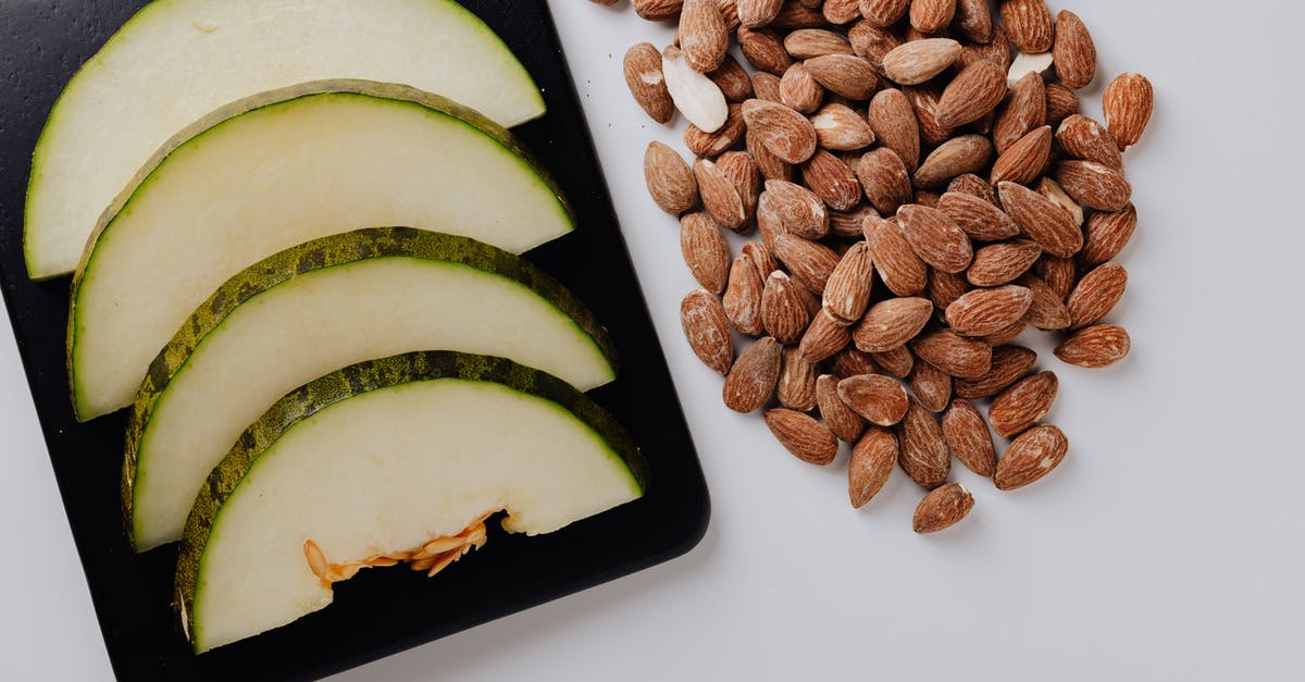 Roast almond for desserts - Pile of almonds and chopped melon on white table Roast almond for desserts - Pile of almonds and chopped melon on white table