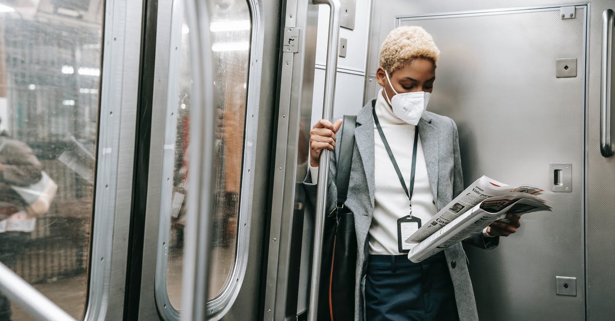 Royal icing safety concern - Concentrated young African American female in formal outfit and protective mask reading fresh newspaper while standing in metro train corner Royal icing safety concern - Concentrated young African American female in formal outfit and protective mask reading fresh newspaper while standing in metro train corner