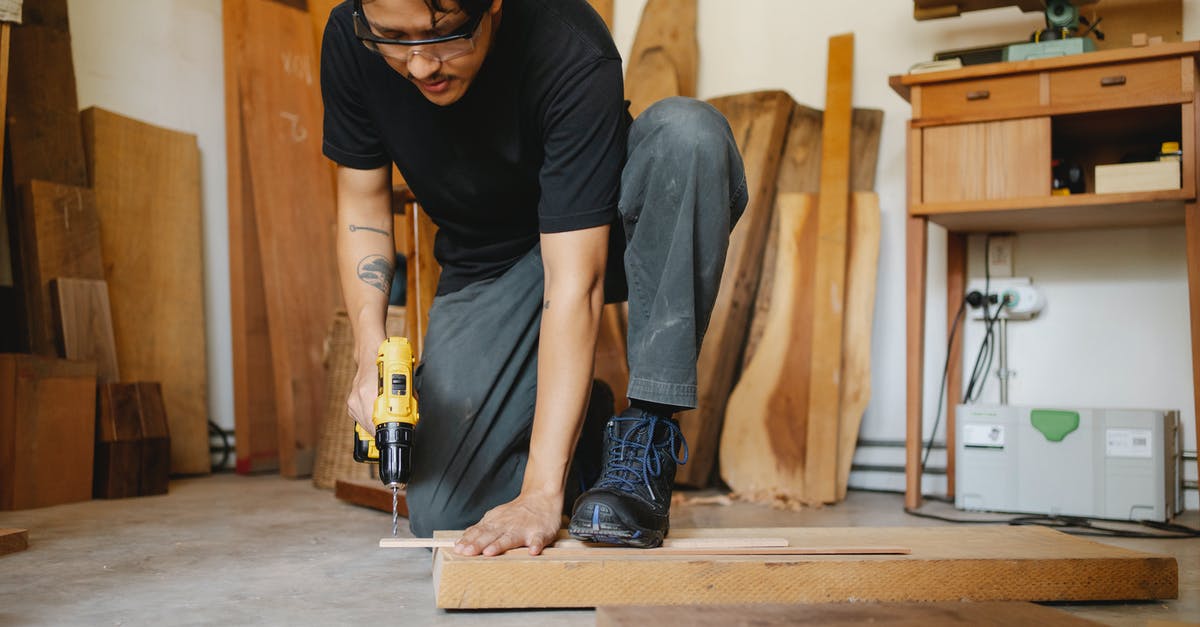 Safety glasses in the kitchen: why are these not common place? - Ethnic man leaning on wooden plank and drilling hole Safety glasses in the kitchen: why are these not common place? - Ethnic man leaning on wooden plank and drilling hole