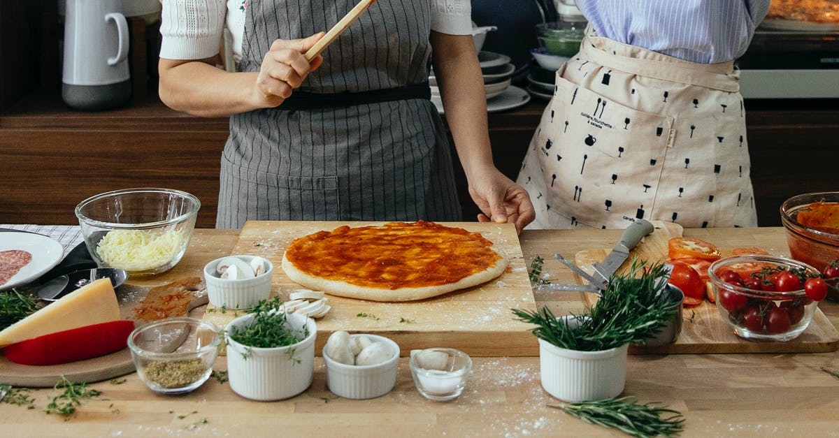 Salting meat before simmering - Crop anonymous female cooks at table with tomato salsa on raw dough near assorted ingredients for pizza in house Salting meat before simmering - Crop anonymous female cooks at table with tomato salsa on raw dough near assorted ingredients for pizza in house
