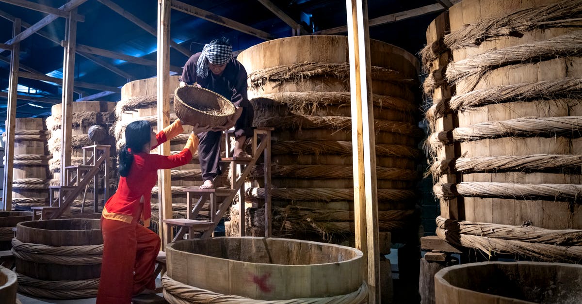 Sauce thickener for large batch - Woman helping male colleague standing on ladder while working in fish sauce factory together Sauce thickener for large batch - Woman helping male colleague standing on ladder while working in fish sauce factory together