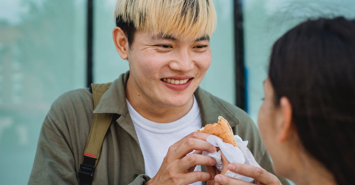 Sausage exploded and looks foamy - Crop woman hand feeding cheerful Asian boyfriend with hot dog Sausage exploded and looks foamy - Crop woman hand feeding cheerful Asian boyfriend with hot dog