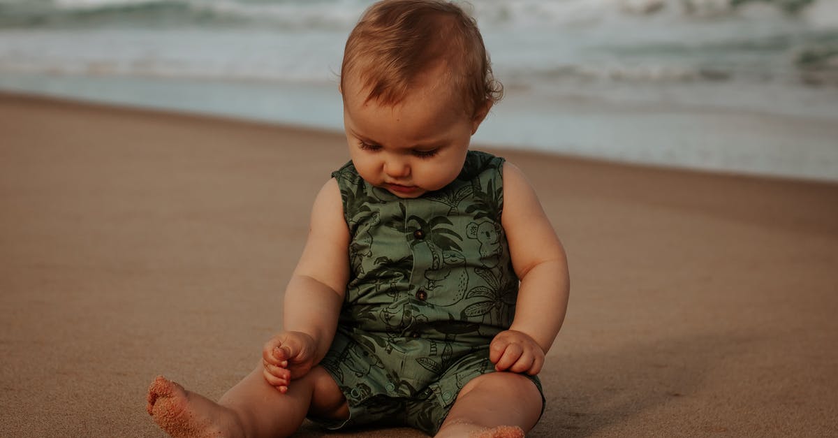 Sausage exploded and looks foamy - Cute baby in ornamental wear resting on sandy sea shore Sausage exploded and looks foamy - Cute baby in ornamental wear resting on sandy sea shore