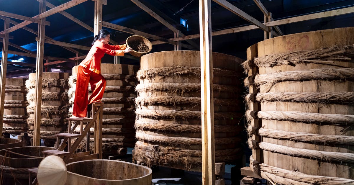 Seasoning a wok, have I burned on the factory oil? - Full body of female adding ingredient from bowl into wooden barrel with fish sauce in factory Seasoning a wok, have I burned on the factory oil? - Full body of female adding ingredient from bowl into wooden barrel with fish sauce in factory