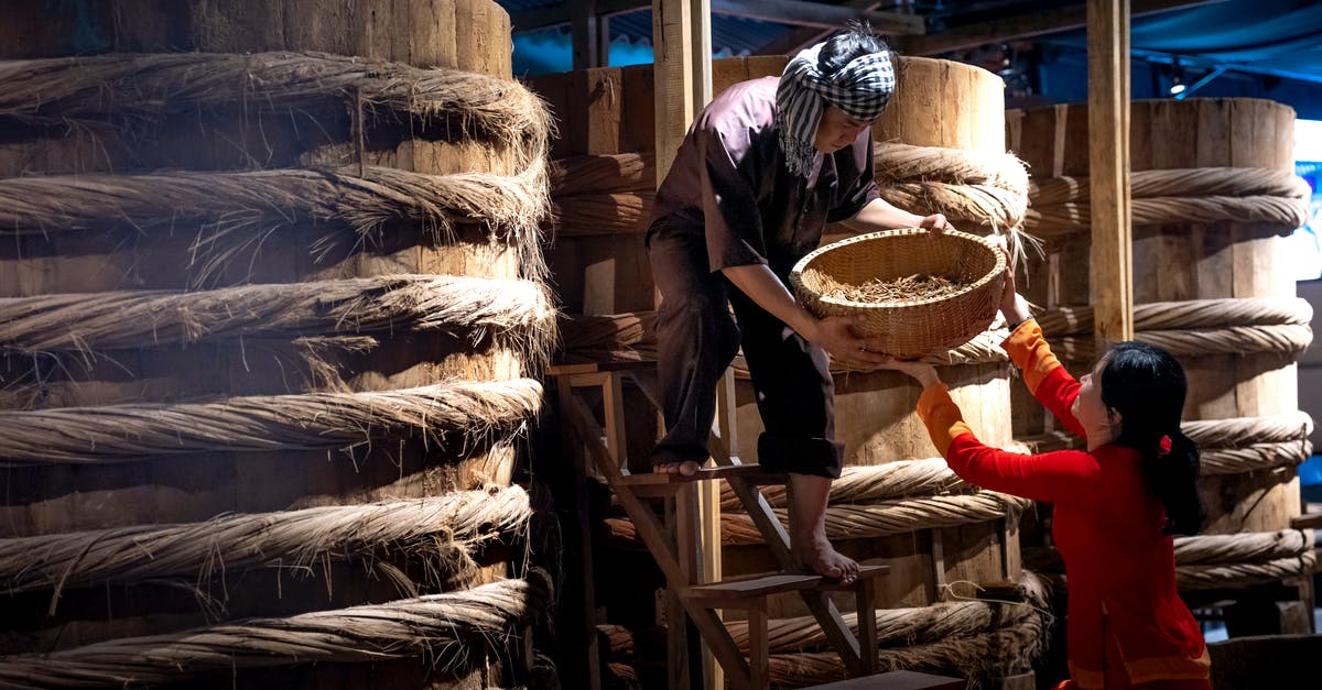 Seasoning a wok, have I burned on the factory oil? - Serious ethnic male worker standing on ladder near barrels with fish sauce while working with colleague Seasoning a wok, have I burned on the factory oil? - Serious ethnic male worker standing on ladder near barrels with fish sauce while working with colleague