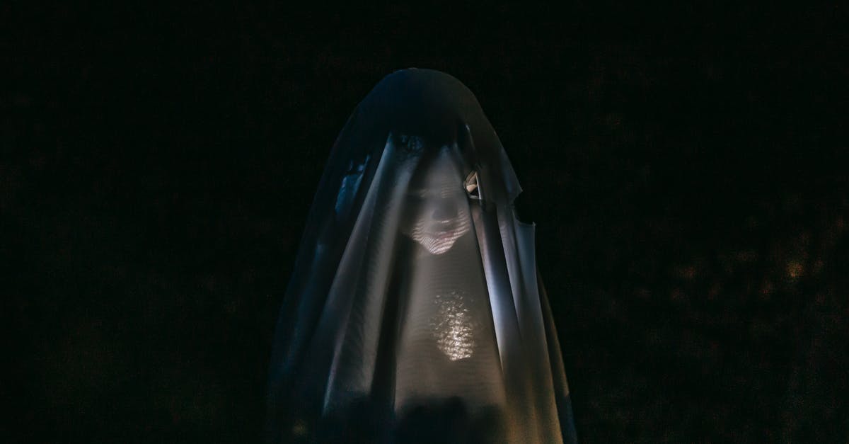Secrets of Gumbo - Mysterious little girl standing in darkness covered with white blanket as ghost and shining flashlight on face Secrets of Gumbo - Mysterious little girl standing in darkness covered with white blanket as ghost and shining flashlight on face