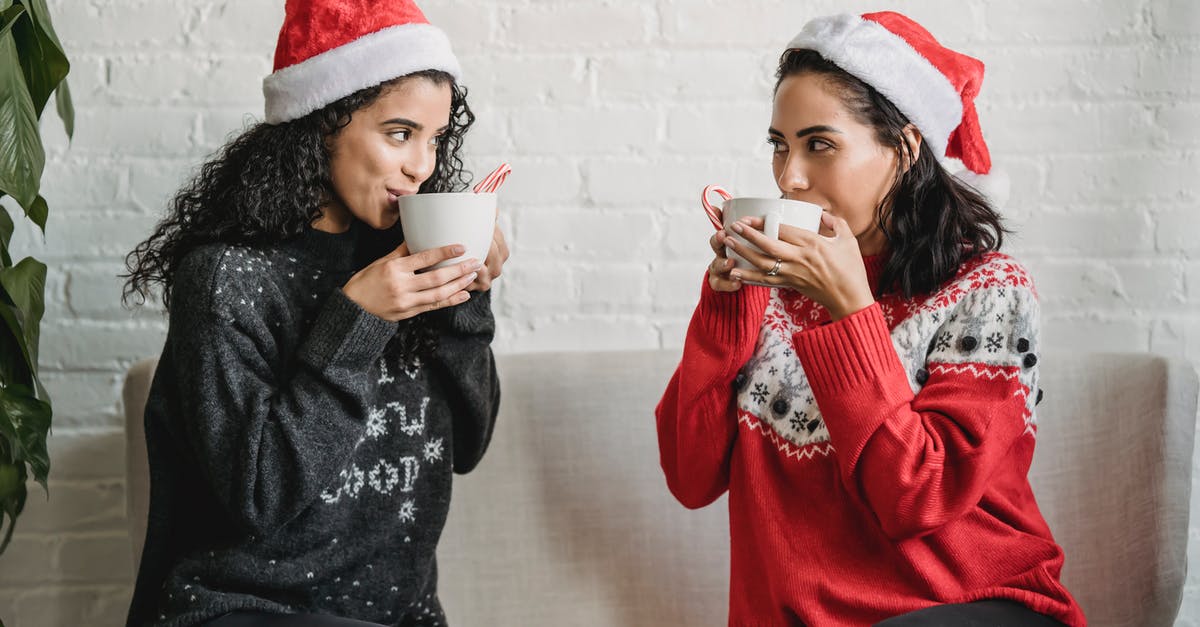 Separating chocolate-coated cookies stuck together - Multiracial girlfriends sitting on sofa at home and drinking cocoa Separating chocolate-coated cookies stuck together - Multiracial girlfriends sitting on sofa at home and drinking cocoa