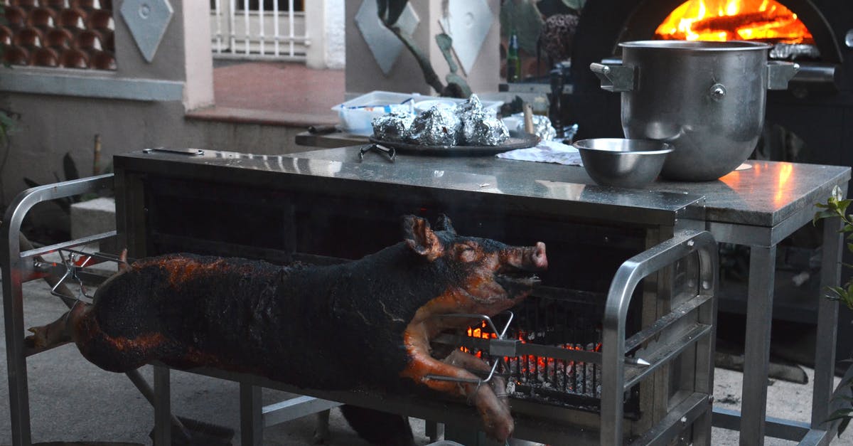 Serving a Whole Pig - Whole smoked pig on broach near metal table with various utensils in yard of countryside house Serving a Whole Pig - Whole smoked pig on broach near metal table with various utensils in yard of countryside house
