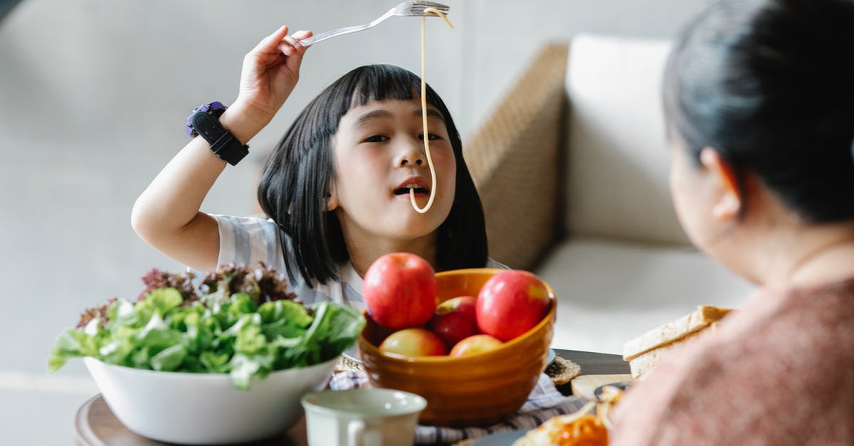 Sheets of fresh pasta sticking together - Cute Asian little girl eating delicious spaghetti while sitting at table with fresh fruits and salad with unrecognizable grandmother Sheets of fresh pasta sticking together - Cute Asian little girl eating delicious spaghetti while sitting at table with fresh fruits and salad with unrecognizable grandmother