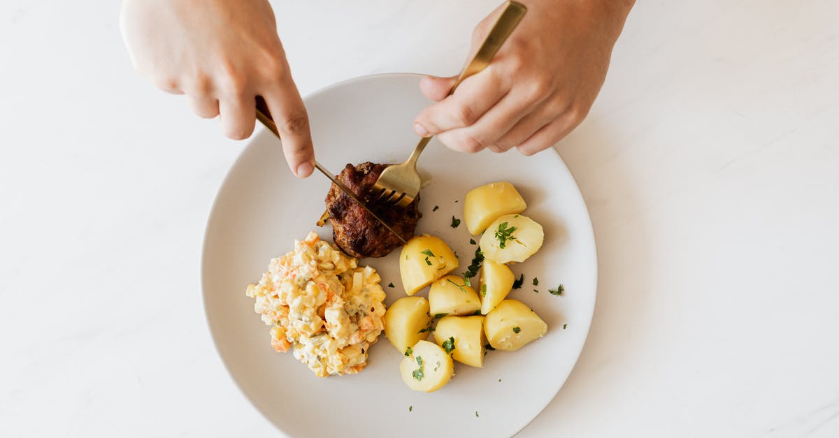 Should beef jerky be cut with or across the grain? - Crop man cutting cutlet on plate with salad and potatoes Should beef jerky be cut with or across the grain? - Crop man cutting cutlet on plate with salad and potatoes