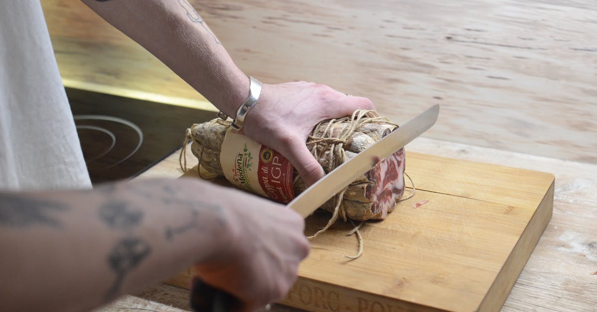 Should beef jerky be cut with or across the grain? - Crop man cutting meat on wooden board at home Should beef jerky be cut with or across the grain? - Crop man cutting meat on wooden board at home