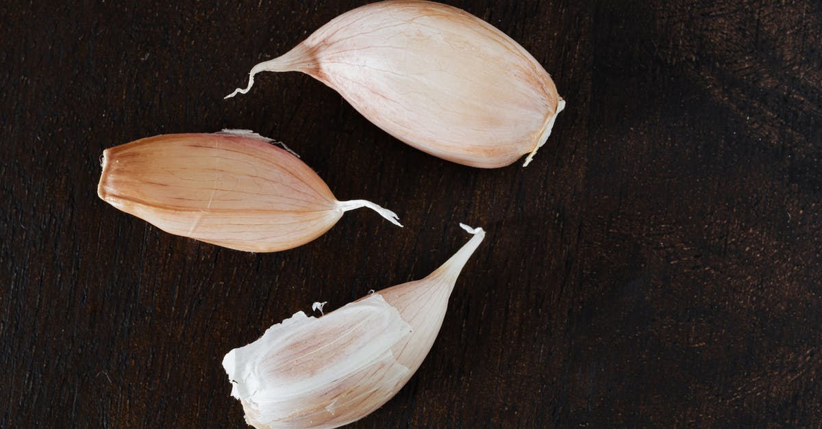 Should one always use the whole garlic clove? - Top view of several cloves of ripe garlic in peel placed on wooden desk during cooking process at home