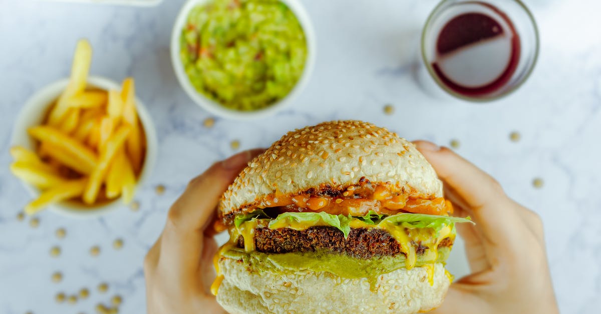 Should Pickle Slices be Above or Below the Hamburger - From above of faceless person eating big hamburger with cutlet between melted cheese and lettuce at table with fast food on blurred background Should Pickle Slices be Above or Below the Hamburger - From above of faceless person eating big hamburger with cutlet between melted cheese and lettuce at table with fast food on blurred background