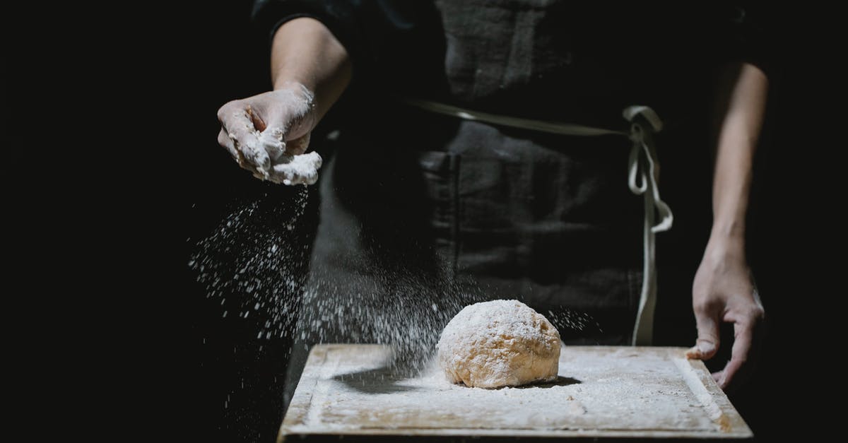 Skills that are only learned by professional chefs? - Unrecognizable baker in uniform standing at table and sprinkling flour in dough while cooking against black background Skills that are only learned by professional chefs? - Unrecognizable baker in uniform standing at table and sprinkling flour in dough while cooking against black background