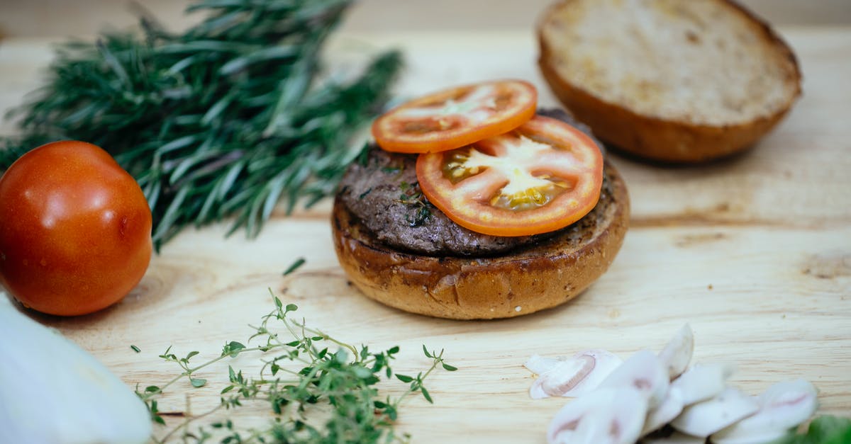 Slow cook beef brisket slices method - Toasted buns with cutlet and tomatoes placed on wooden table with greens and mushroom in kitchen while preparing tasty burger Slow cook beef brisket slices method - Toasted buns with cutlet and tomatoes placed on wooden table with greens and mushroom in kitchen while preparing tasty burger