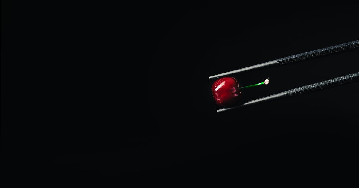 Small black specks on wok food - Shiny black colored tweezers with bright vinous glossy cherry with green stem on black background Small black specks on wok food - Shiny black colored tweezers with bright vinous glossy cherry with green stem on black background