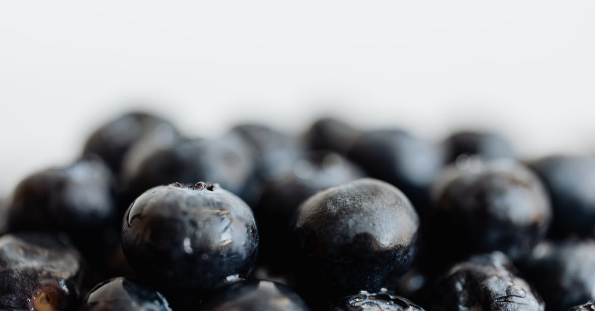 Small black specks on wok food - Closeup bunch of ripe delicious fresh ripe blueberries placed on white surface Small black specks on wok food - Closeup bunch of ripe delicious fresh ripe blueberries placed on white surface