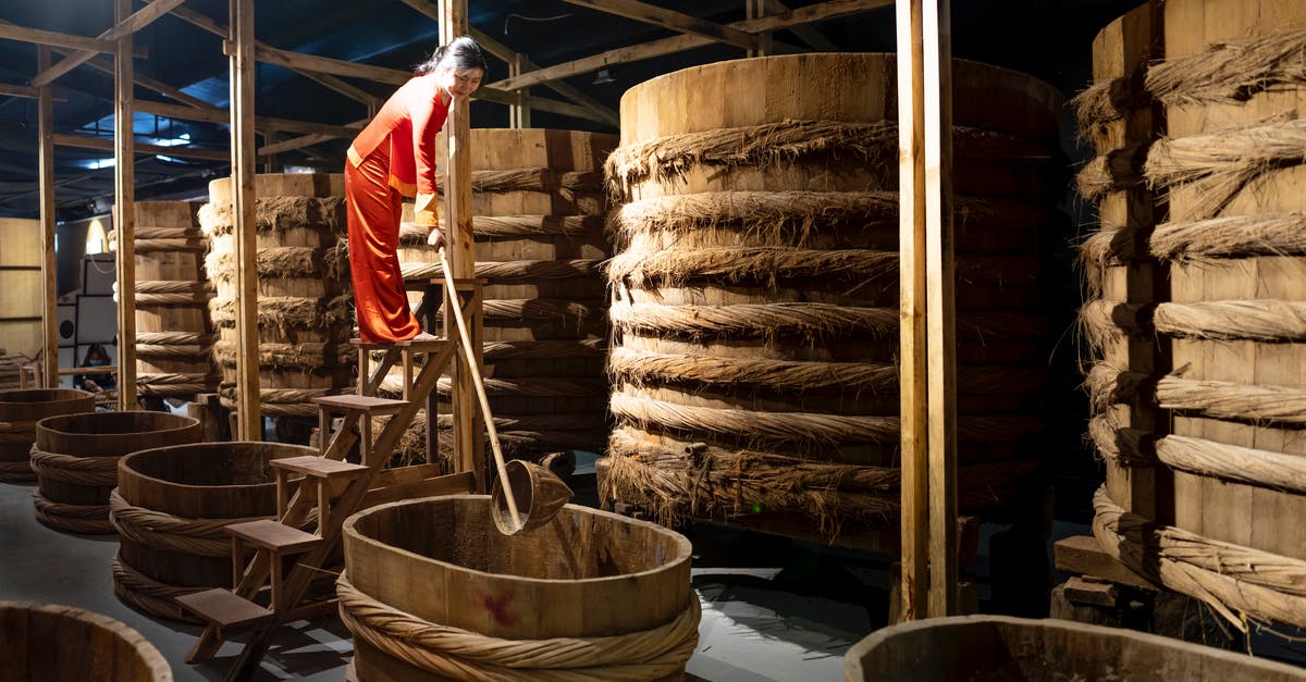 Soy Sauce storage container - Full body of Asian female worker with instrument standing near row of barrels in fish sauce factory Soy Sauce storage container - Full body of Asian female worker with instrument standing near row of barrels in fish sauce factory