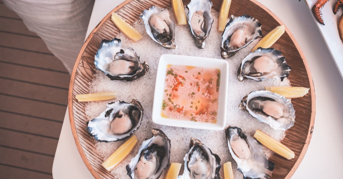 Spotting frozen seafood in restaurants - From above of wooden tray with fresh raw oysters served on table with mignonette sauce and lemon slices on chopped ice on yacht Spotting frozen seafood in restaurants - From above of wooden tray with fresh raw oysters served on table with mignonette sauce and lemon slices on chopped ice on yacht