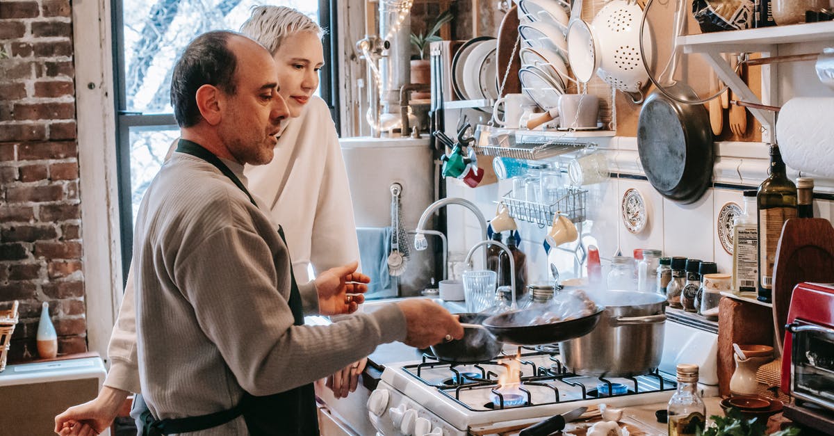 Stainless steel pan - Concentrated husband in apron frying food on pan while cooking on gas stove with wife in kitchen Stainless steel pan - Concentrated husband in apron frying food on pan while cooking on gas stove with wife in kitchen
