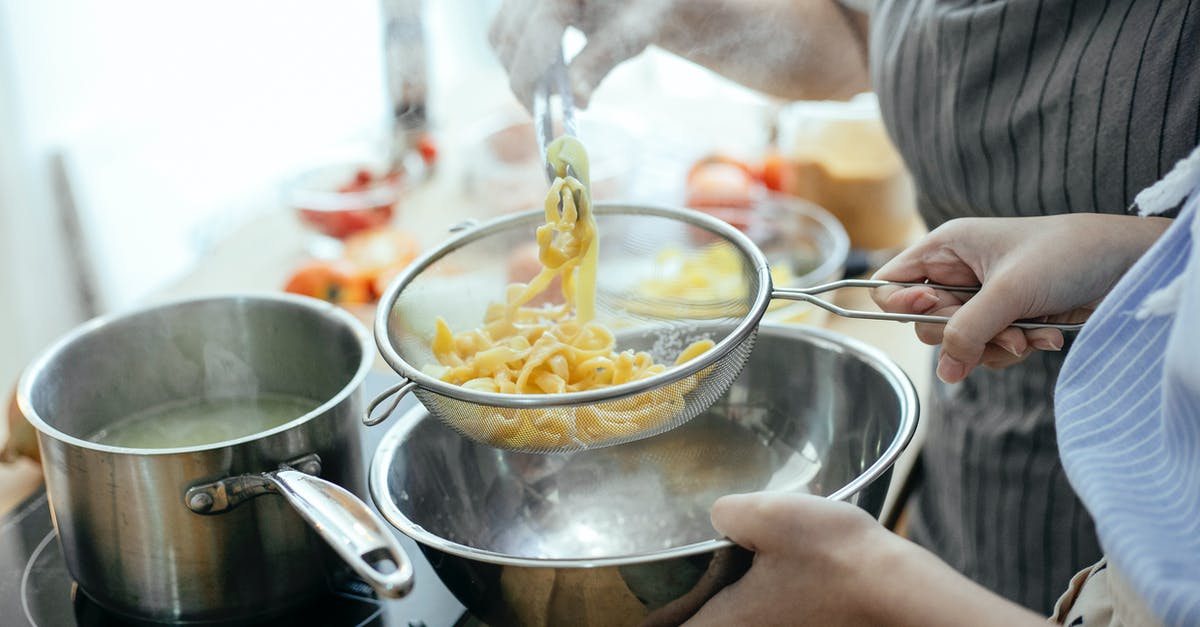 Steam pudding in square bowl - High angle of crop faceless female chefs putting noodles from saucepan with boiling water into strainer while standing at table with ingredients in kitchen Steam pudding in square bowl - High angle of crop faceless female chefs putting noodles from saucepan with boiling water into strainer while standing at table with ingredients in kitchen