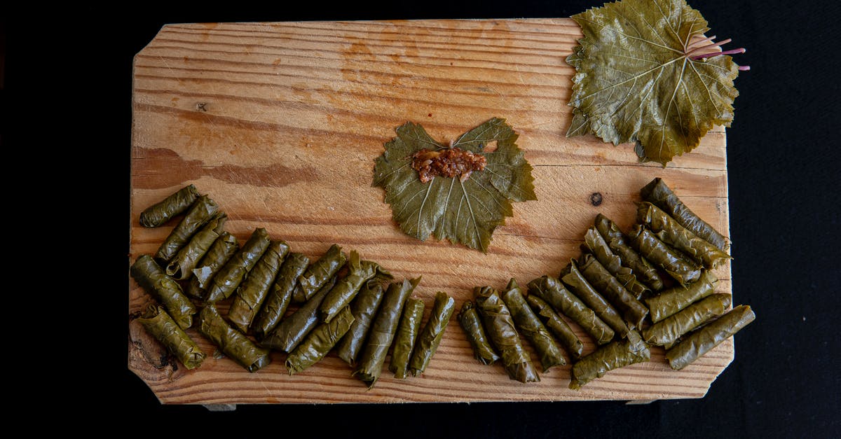 Subsitute in this kale and grape recipe - Top view of sarma rolls near vine leaves with meat filling on wooden table on black background Subsitute in this kale and grape recipe - Top view of sarma rolls near vine leaves with meat filling on wooden table on black background