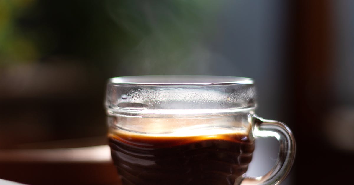 Substitute instant coffee for brewed black coffee - Delicious aromatic black coffee with steam in creative design glass cup with shiny surface on table for breakfast on blurred background Substitute instant coffee for brewed black coffee - Delicious aromatic black coffee with steam in creative design glass cup with shiny surface on table for breakfast on blurred background
