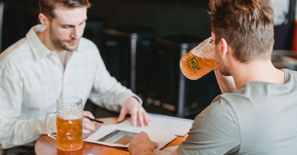Substitution of root beer concentrate for extract - Focused colleagues drinking glasses with beer at table with papers and tablet with black screen on blurred background Substitution of root beer concentrate for extract - Focused colleagues drinking glasses with beer at table with papers and tablet with black screen on blurred background