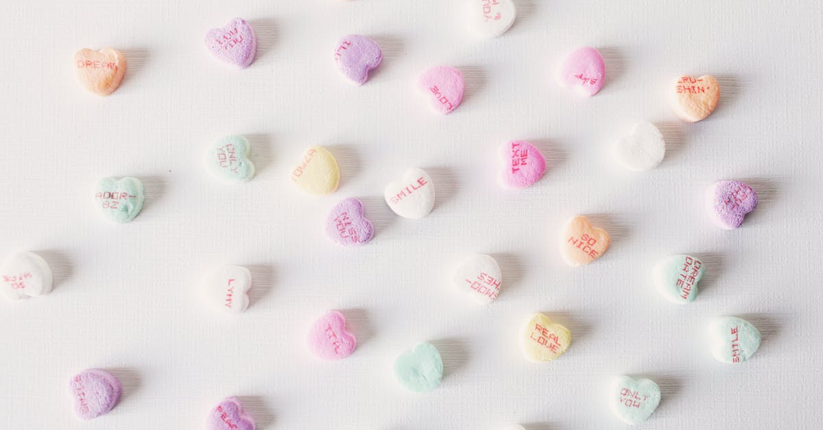 Sweet plums going tart as I chew - Top view composition of multicolored small heart shaped sweets placed on plain white surface Sweet plums going tart as I chew - Top view composition of multicolored small heart shaped sweets placed on plain white surface