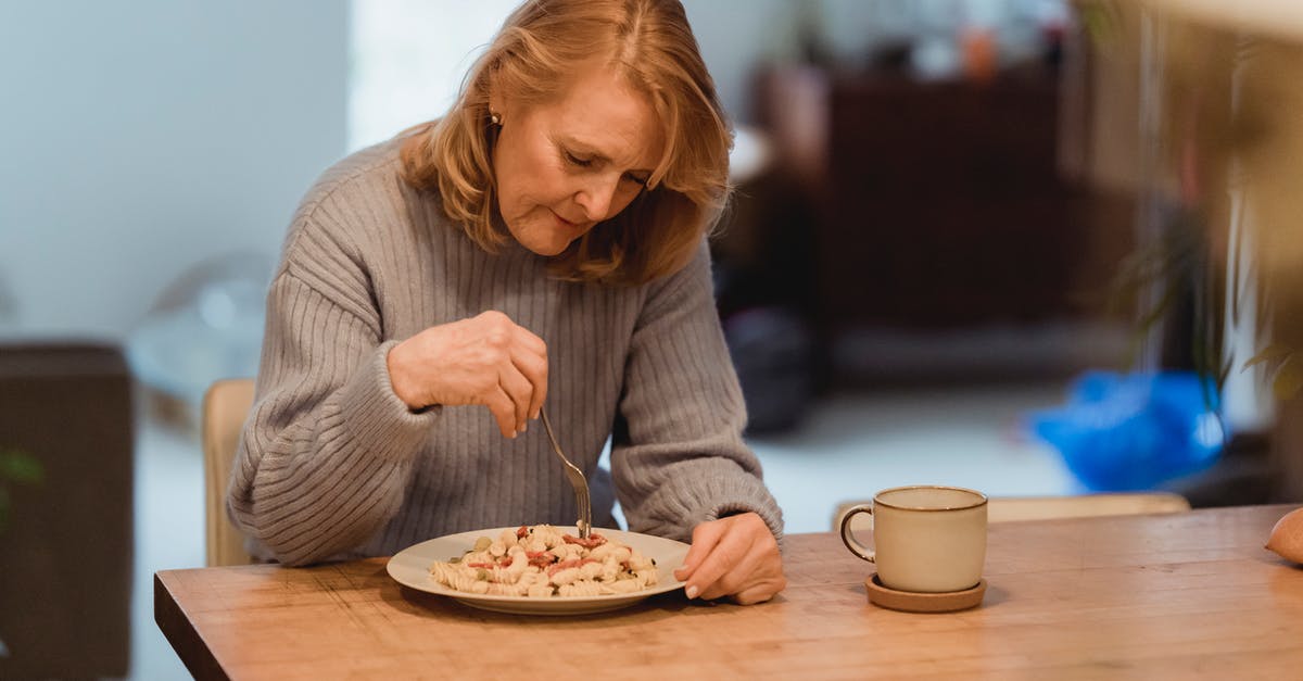 Tea taste changes if watered down after steeping - Emotionless senior female wearing blue sweater enjoying yummy vegetable pasta while sitting at table in living room Tea taste changes if watered down after steeping - Emotionless senior female wearing blue sweater enjoying yummy vegetable pasta while sitting at table in living room