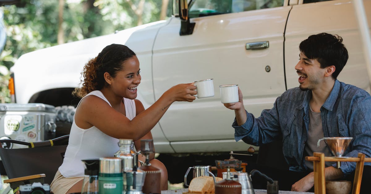 the whistle on the kettle keeps popping off - Joyful young diverse couple clinking coffee cups during picnic in nature the whistle on the kettle keeps popping off - Joyful young diverse couple clinking coffee cups during picnic in nature